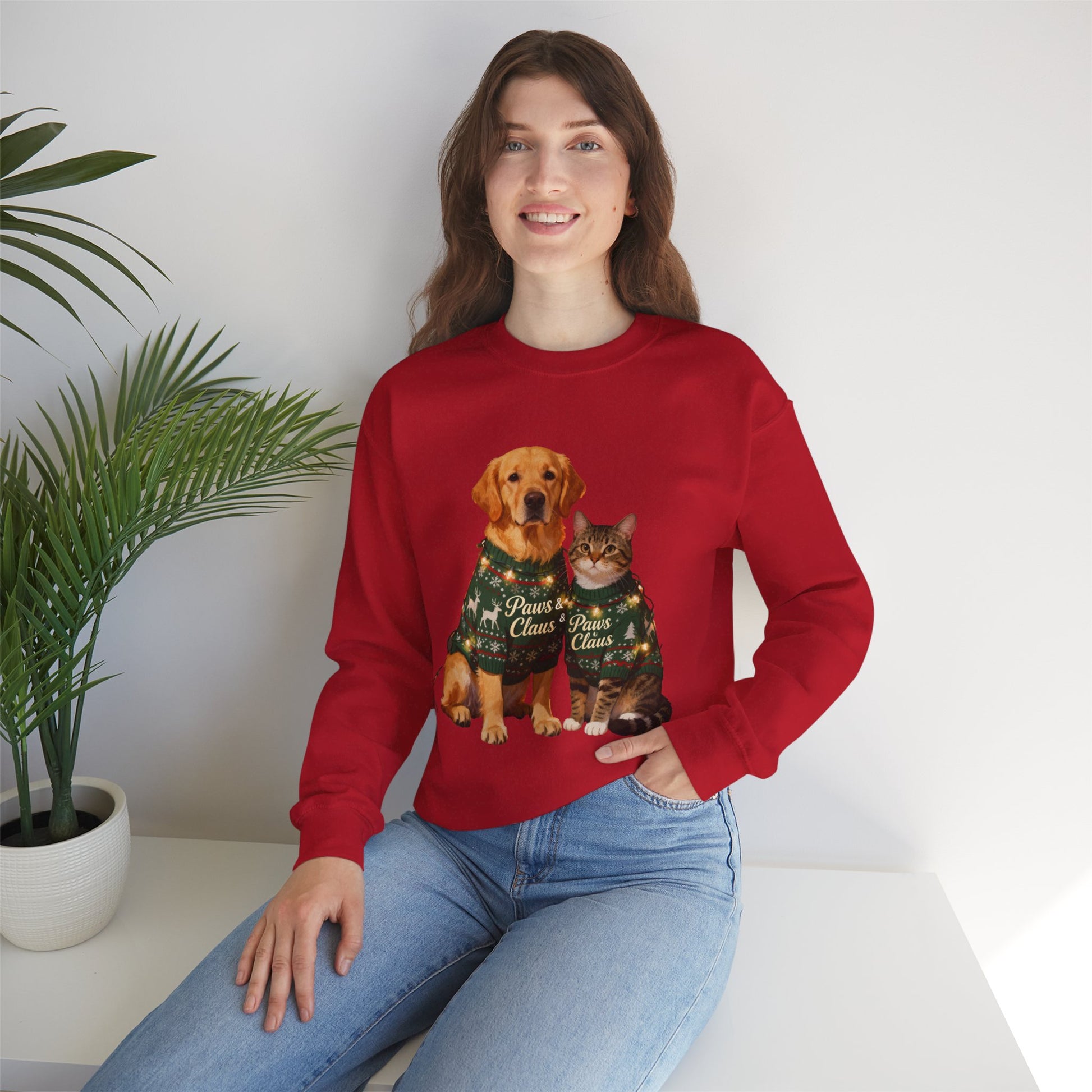 Person wearing a red sweatshirt with a dog and cat design, sitting on a white surface with a plant in the background.